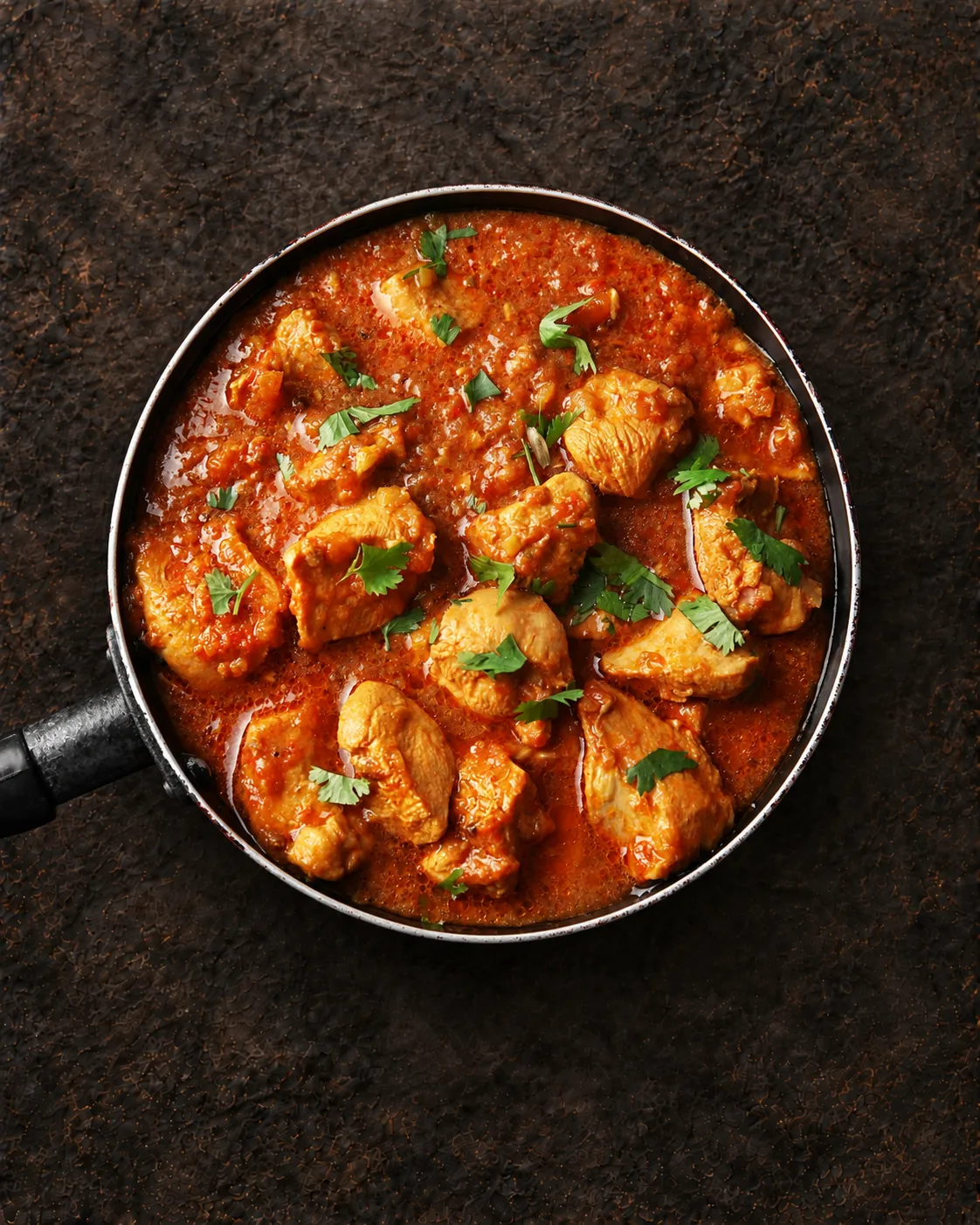 Chicken curry simmering in a pan with fresh coriander